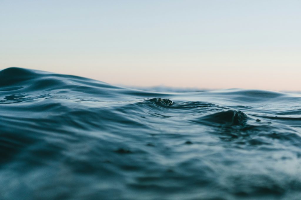 Dunkelblaues Wasser mit einem Abendhimmel im Hintergrund. Das Wasser zeigt leicht Wellen. Der Himmel ist orange und blau.